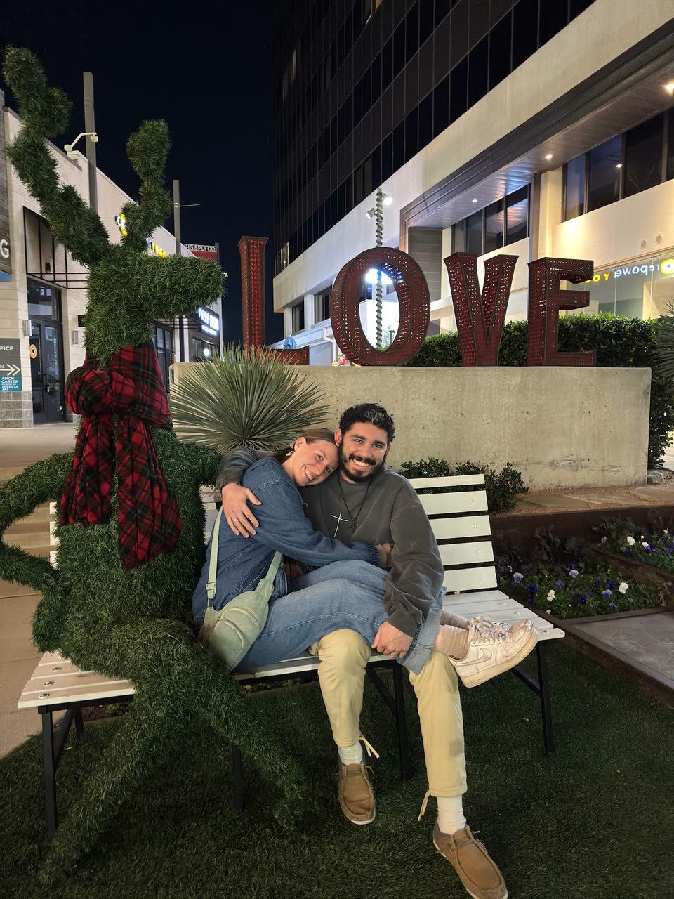 Andrew and Hailey sitting together beneath an illuminated LOVE sign