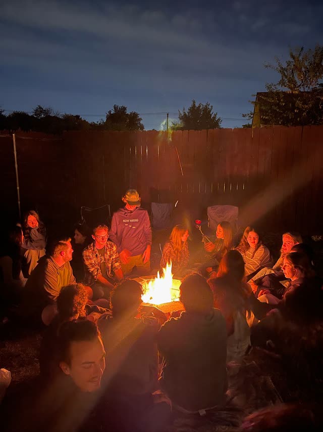 A large group of friends seated around a backyard fire