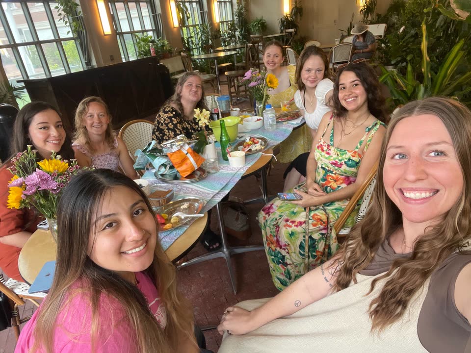 Hailey smiling with friends around a table with flowers and food